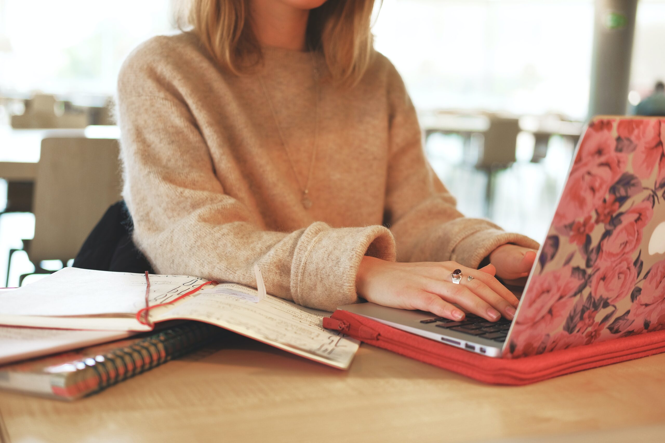Woman in brown sweater typing on laptop with floral cover